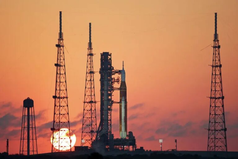 NASA SLS rocket with Orion capsule on Launch Pad 39B at Kennedy Space Center, silhouetted against a vivid orange sunset sky, ahead of the Artemis 2 mission launch in April 2026.