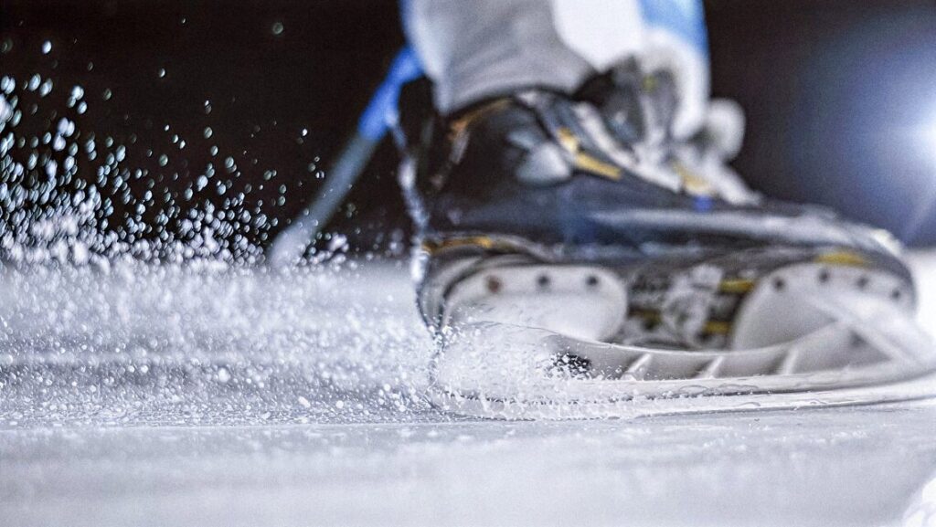 Close-up of an ice skate blade spraying ice particles on a rink, illustrating why ice is slippery due to its quasi-liquid surface layer
