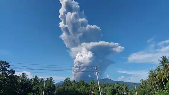 Massive white ash column rising 10 kilometers into blue sky from Mount Dukono volcano eruption on Halmahera Island, Indonesia, viewed over palm trees and power lines, May 8, 2026.