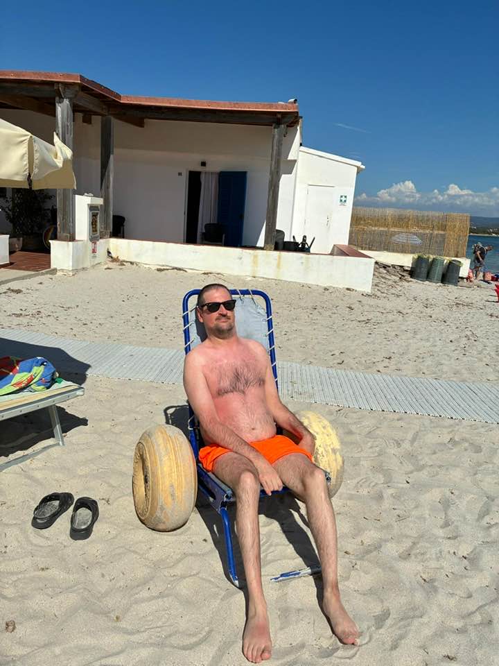 Man relaxing on a beach wheelchair with balloon wheels on the white sand of Velmarì, Fertilia waterfront, Sardinia.