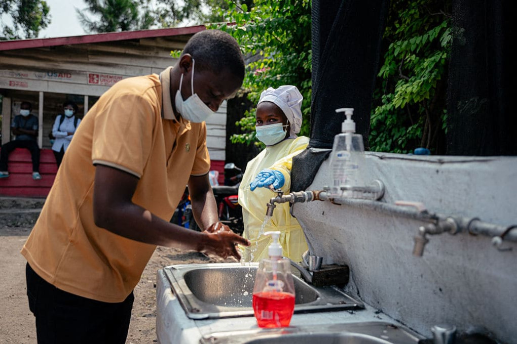 Health worker assists man washing hands at Ebola prevention station outside Goma hospital, DRC, May 2026.